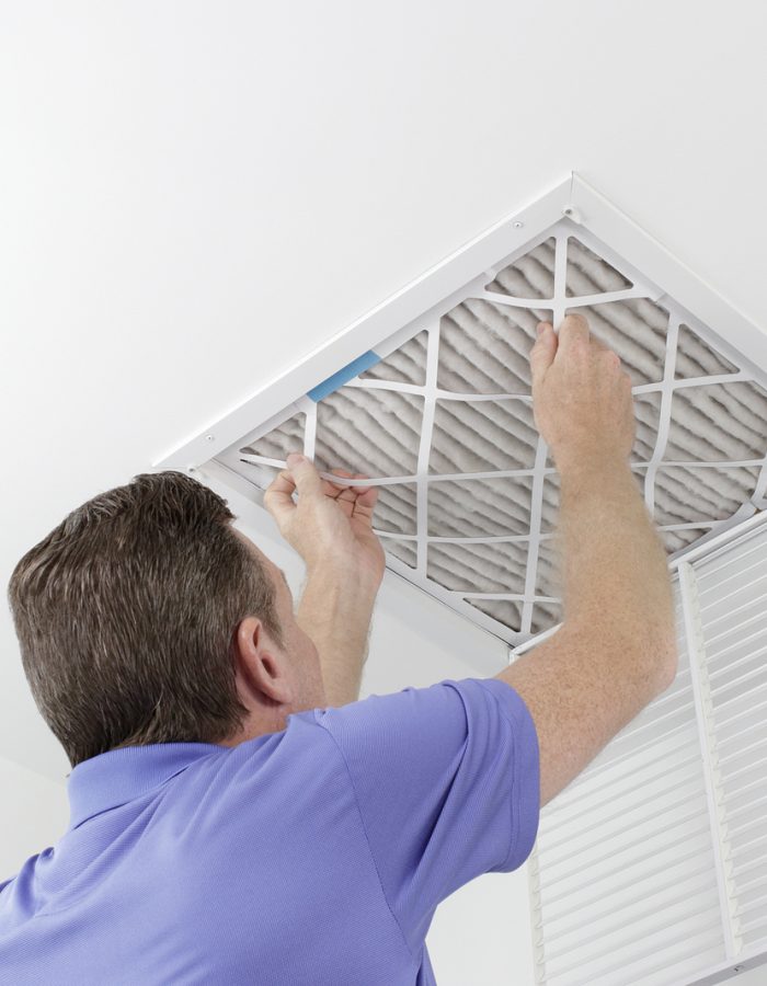 Caucasian male removing a square pleated dirty air filter with both hands from a ceiling air duct. Guy taking out an unclean air filter from a home ceiling air vent.